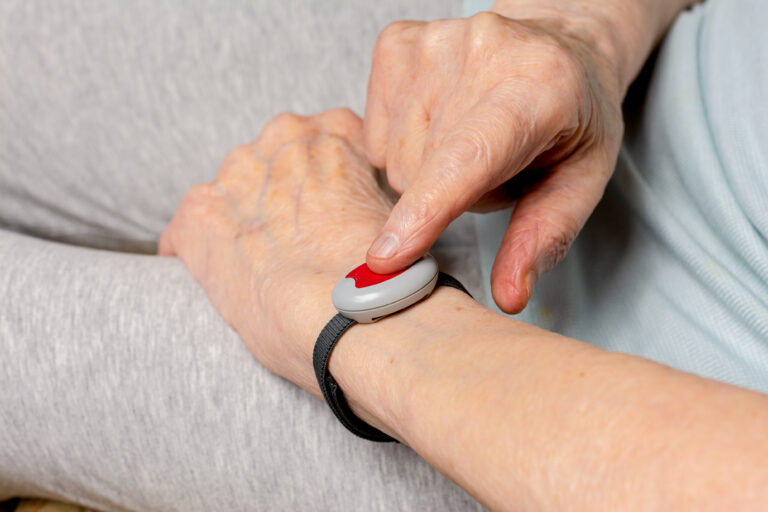 Femme âgée portant une montre de téléassistance et appuyant sur le bouton d’alerte pour demander de l’aide.