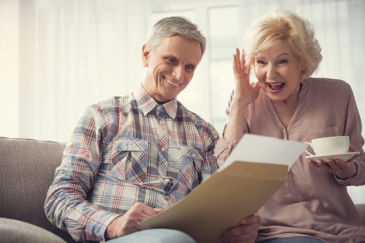 Un couple de seniors souriant devant leur feuille d'impôt, heureux de profiter d'un crédit d'impôt.